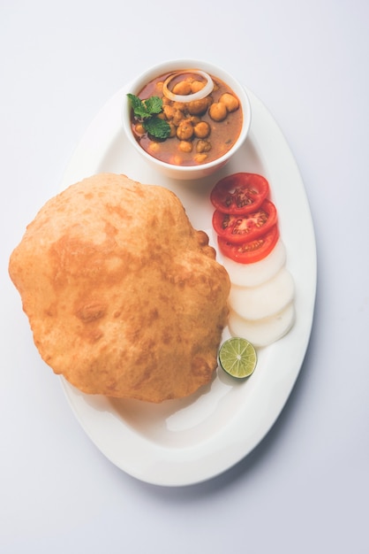 Chole Bhature o curry di ceci e puri fritti serviti in stoviglie di terracotta su sfondo bianco. messa a fuoco selettiva