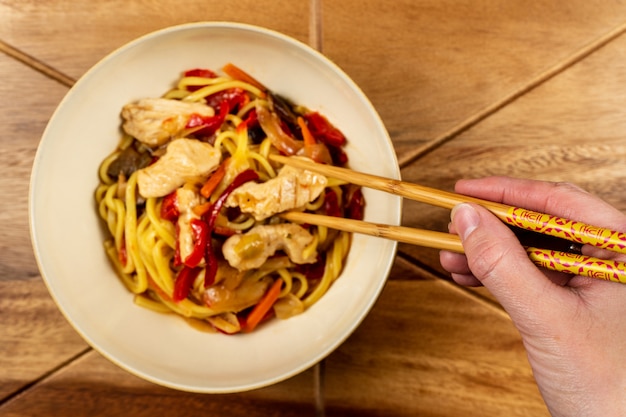 Chow mein di pollo e bacchette sul tavolo di legno