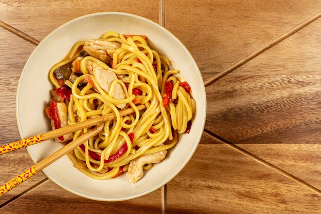 Chow mein di pollo e bacchette sul tavolo di legno