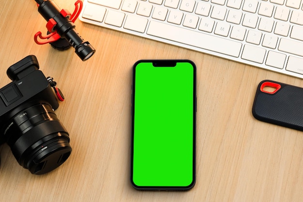 Chroma Key sullo schermo dello smartphone sul tavolo di legno. Ambiente creatore di contenuti con tastiera, fotocamera e microfono. Schermo verde.