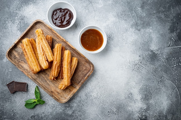 Churros con zucchero e salsa al cioccolato, su sfondo grigio, vista dall'alto laici piatta con spazio per testo, copyspace