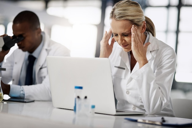 Ci deve essere una cura per il comune mal di testa Inquadratura ritagliata di una scienziata matura che soffre di mal di testa mentre lavora nel suo laboratorio di ricerca