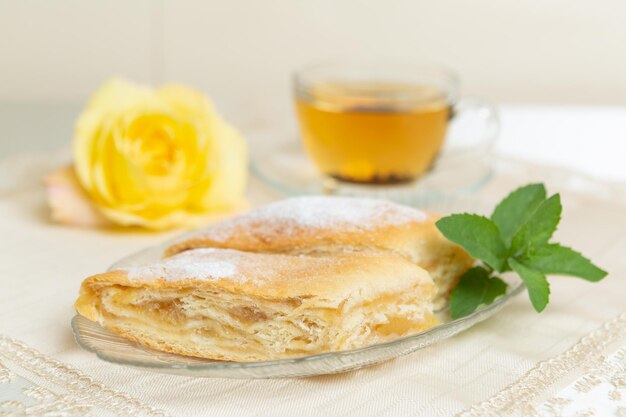 Ci sono due fette di torta di mele, mirtilli e foglie di menta sul piatto una tazza di tè accanto e il tavolo è decorato con una rosa viva