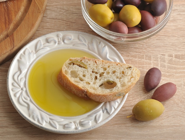 Ciabatta di pane a fette su tavola rotonda, olive e olio extra vergine di oliva