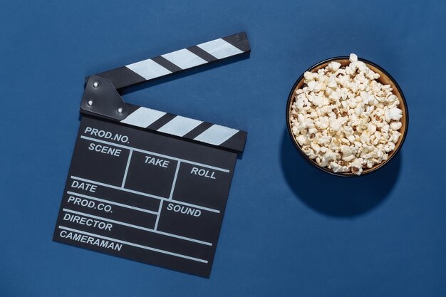 Ciak di film, ciotola di popcorn su sfondo blu classico con ombre profonde. Industria dell'intrattenimento. Vista dall'alto