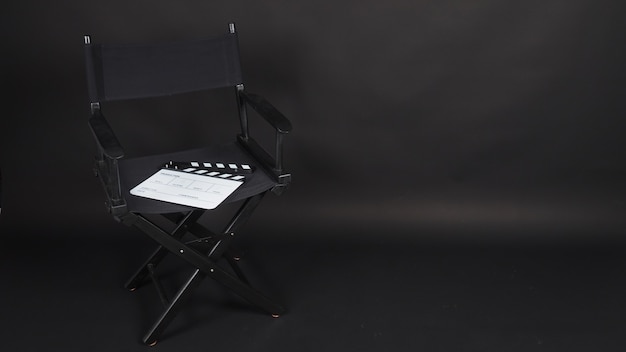 Ciak o clap board o ardesia cinematografica con sedia da regista utilizzata nella produzione di video, film, industria cinematografica su sfondo nero.