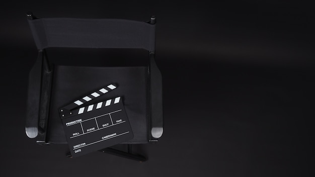 Ciak o clap board o ardesia cinematografica con sedia da regista utilizzata nella produzione di video, film, industria cinematografica su sfondo nero.