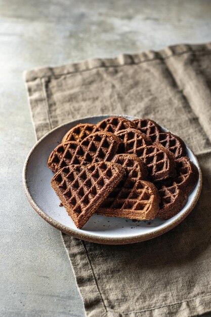 Cialde al cioccolato a forma di cuore in piatto di ceramica su sfondo testurizzato con tovaglia di lino, natura morta per san valentino