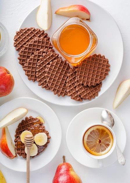 Cialde al cioccolato con pera rossa, miele e banana per colazione su sfondo bianco.