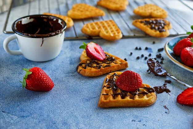 Cialde belghe a forma di cuori con fragole fresche e topping al cioccolato su tavola blu