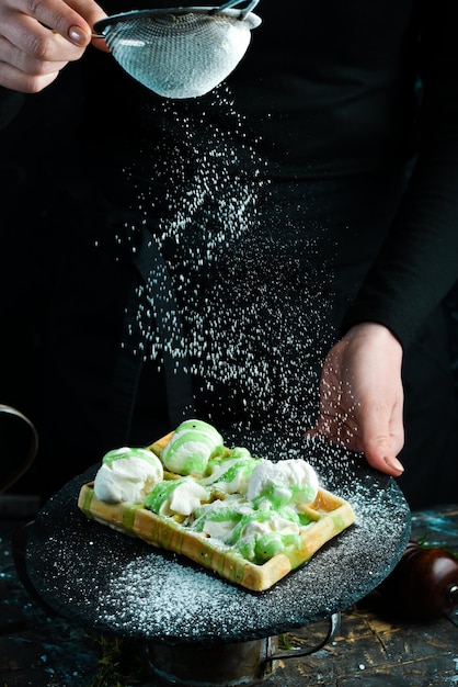 Cialde belghe con gelato, panna e salsa di kiwi. Su uno sfondo nero.