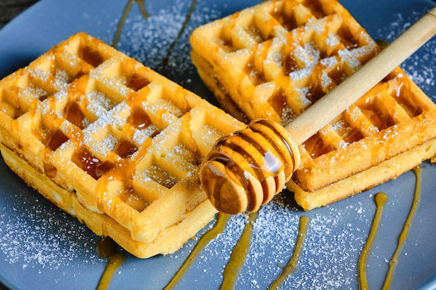 Cialde dolci cosparse di miele e cosparse di zucchero a velo su un piatto blu