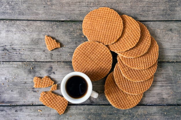 Cialde olandesi tradizionali con caramello e tazza di caffè sullo sfondo di legno, vista dall'alto.