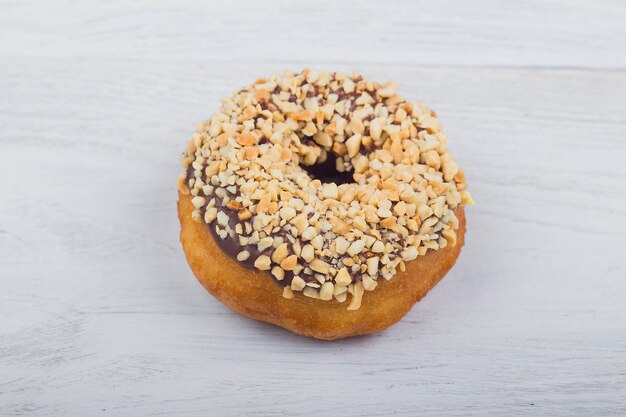 Ciambella al cioccolato cosparsa di noci su fondo di legno bianco