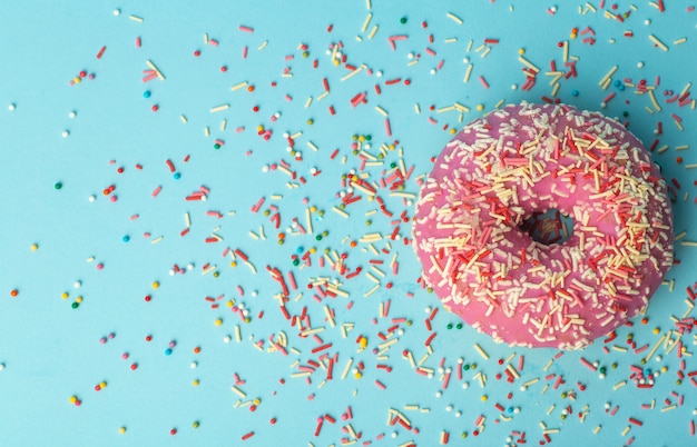 Ciambella (ciambella) di diversi colori su uno sfondo blu con spruzzi di zucchero festivo multicolore. Vacanze e dolci, cottura per bambini, concetto di zucchero