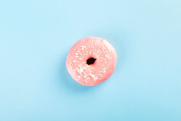 Ciambella con glassa rosa e guarnizione della pasticceria della noce di cocco sul fondo blu