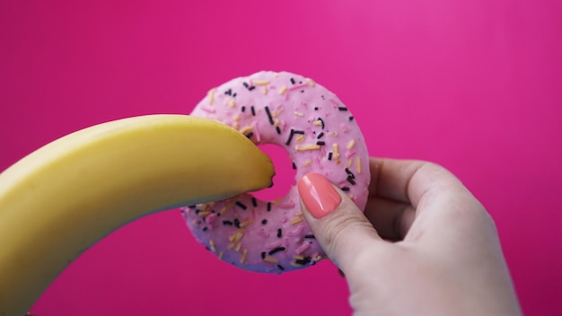 Ciambella dolce e banana in mano su sfondo di colore rosa. Concetto di sesso ed erotico