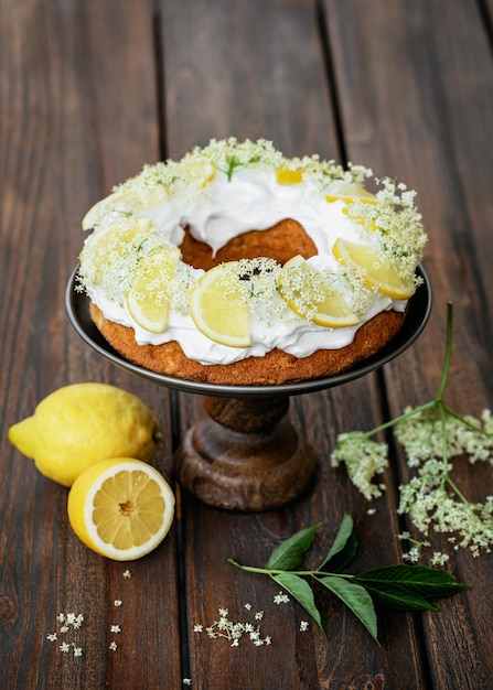 Ciambella fatta in casa, su centrino con glassa di zucchero, fettine di limone e fiori di sambuco