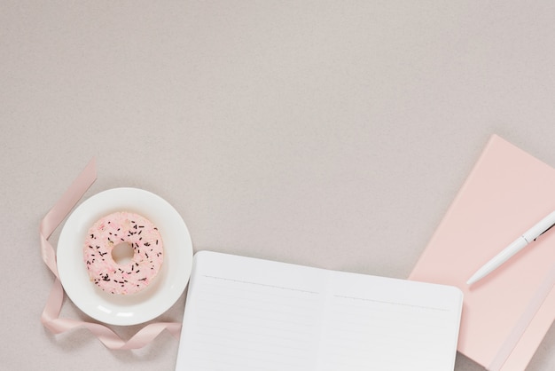 Ciambella rosa su un piatto bianco e un diario rosa con una penna, taccuino con pagine pulite