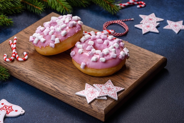 Ciambella smaltata rosa e marshmallow con decorazioni natalizie su un tagliere di legno