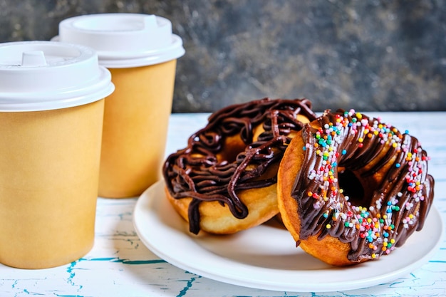 Ciambelle al cioccolato e caffè da asporto su uno sfondo scuro.