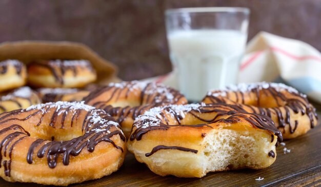 Ciambelle classiche fatte in casa con scaglie di cioccolato e cocco e un bicchiere di latte su uno sfondo di legno scuro. Avvicinamento.