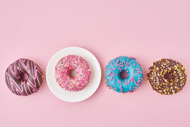 Ciambelle colorate diverse e piastra sulla superficie rosa. Concetto di cibo creativo