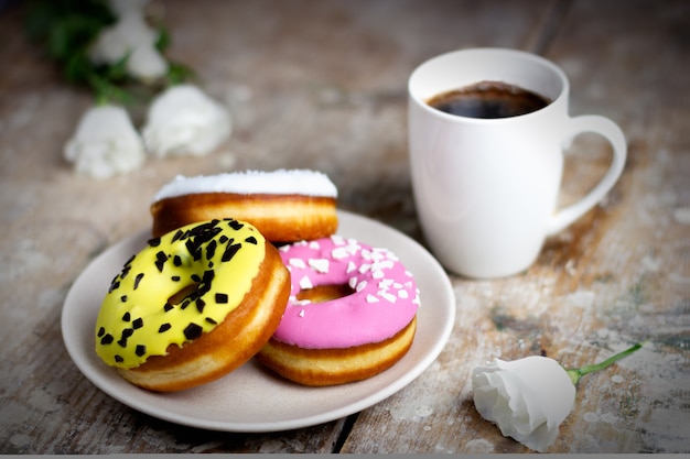 Ciambelle colorate su un piatto con una tazza di caffè su un tavolo di legno fiori leggeri si trovano nelle vicinanze