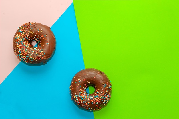 Ciambelle con glassa al cioccolato e confettini colorati di forma tonda su fondo colorato