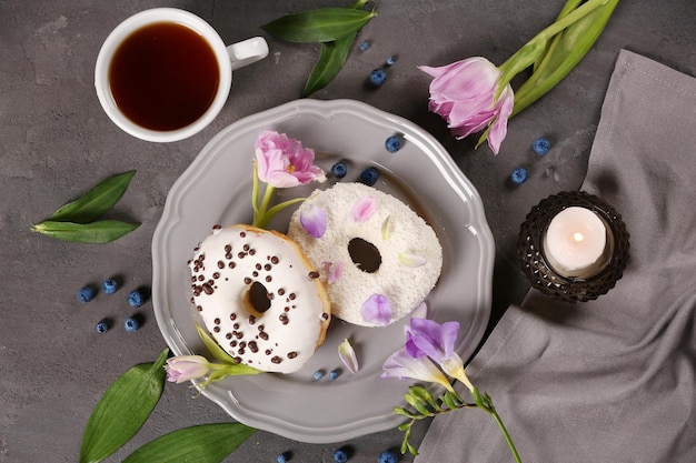 Ciambelle deliziose tazza di caffè e fiori sul tavolo grigio