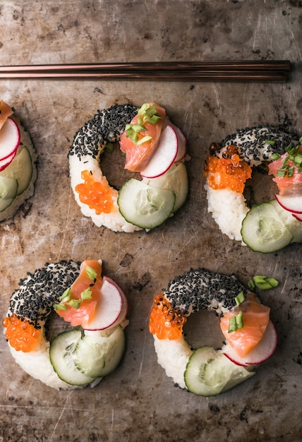 Ciambelle di sushi con salmone, cetriolo e ravanello sulla vista superiore della superficie scura. Alimenti ibridi.