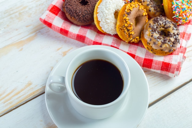 Ciambelle e caffè su uno sfondo di legno bianco.