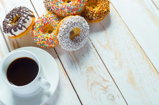 Ciambelle e caffè su uno sfondo di legno bianco.