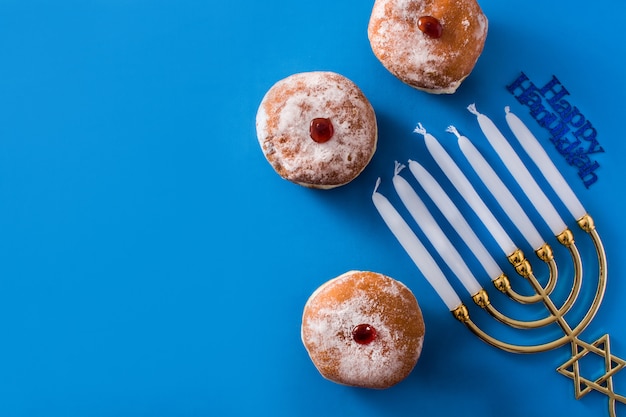 Ciambelle ebree del menorah e di sufganiyot di Chanukah sul copyspace blu di vista superiore