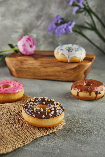 Ciambelle multicolori con glassa e spruzza con fiori su sfondo grigio.