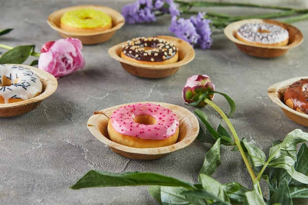 Ciambelle multicolori con glassa e spruzza con fiori su sfondo grigio.