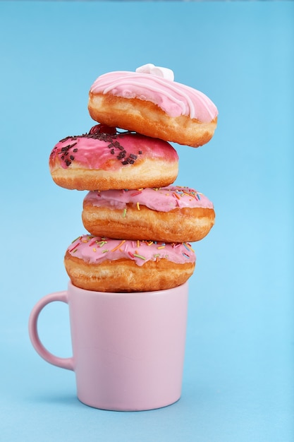 Ciambelle rosa dolci con una tazza rosa su sfondo blu. Concept dessert, dolce vita, siamo ciò che mangiamo. Sfondo blu, copia spazio.