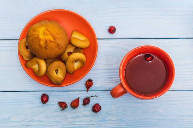 Ciambelle rotonde fatte in casa con muffin in un piatto d'arancia e tè alla rosa canina Idea per una deliziosa colazione