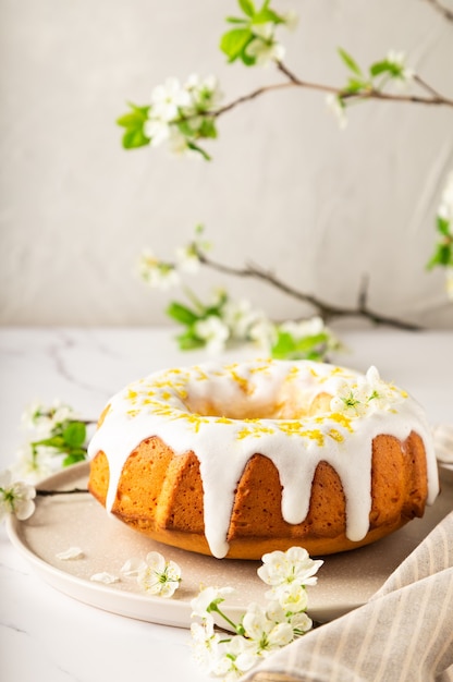 Ciambellone al limone fatto in casa decorato con glassa bianca e scorza su fondo di marmo bianco