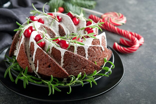 Ciambellone natalizio al cioccolato Torta tradizionale alla frutta natalizia con glassa bianca mirtilli rossi e rosmarino su sfondo scuroDecorazione natalizia Cottura invernale a Natale o Capodanno Copia spazio