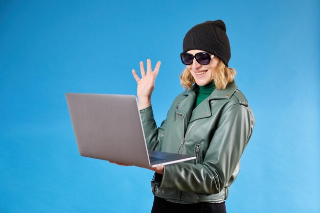 Ciao Bella donna con i capelli biondi che agita la mano salutando la videochiamata sullo schermo del laptop con un amico che comunica online Scatto in studio al coperto isolato su sfondo blu