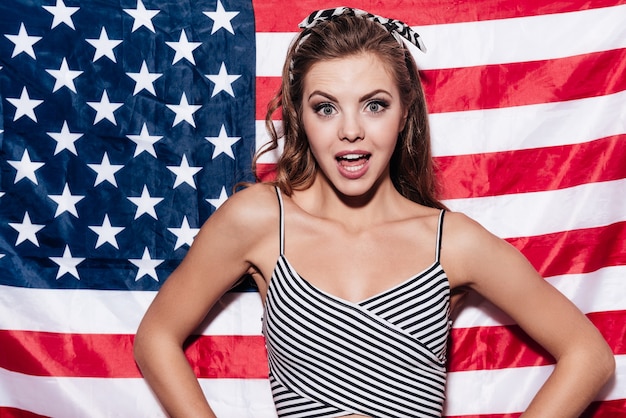 Ciao dagli Stati Uniti! Bella giovane donna in piedi contro la bandiera nazionale americana