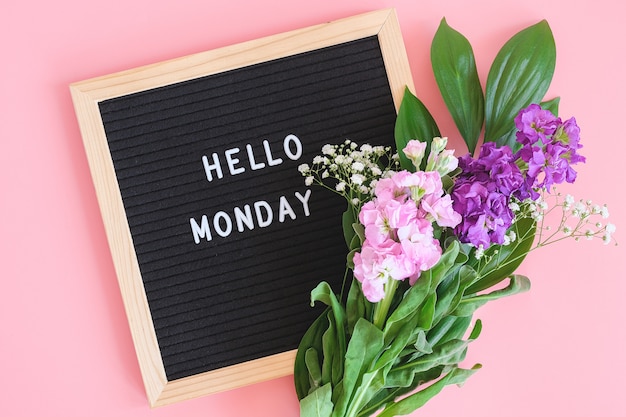 Ciao lunedì testo sulla lavagna nera e bouquet di fiori colorati su sfondo rosa.