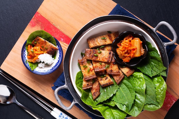 Cibo asiatico concetto fatto in casa coreano alla griglia pancia di maiale BBQ Samgyeopsalgui con kimchi e shiso e insalata su sfondo nero con spazio di copia