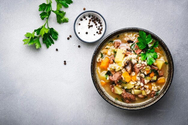 Cibo autunnale Zuppa riscaldante con funghi zucca verdure manzo e orzo Vista dall'alto dello sfondo grigio del tavolo