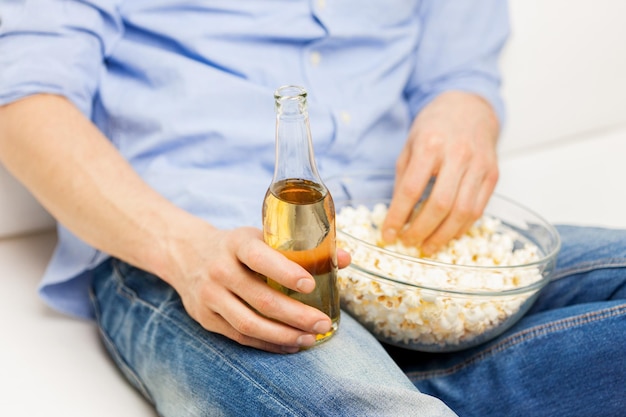 cibo, cibo spazzatura, alimentazione malsana e concetto di persone - primo piano dell'uomo con popcorn e bottiglia di birra a casa