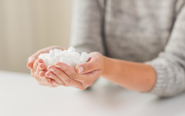 cibo, cibo spazzatura, diabete e concetto di alimentazione malsana - primo piano di zucchero bianco in zollette nelle mani di una donna