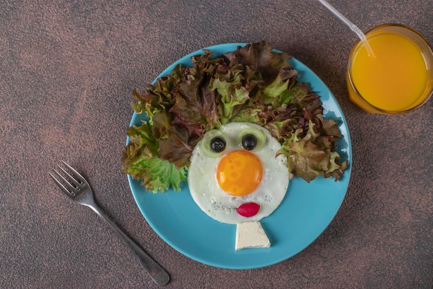 Cibo divertente per bambini faccina sorridente a base di uova fritte cetrioli ravanelli e foglie di lattuga Colazione sana e creativa per bambini