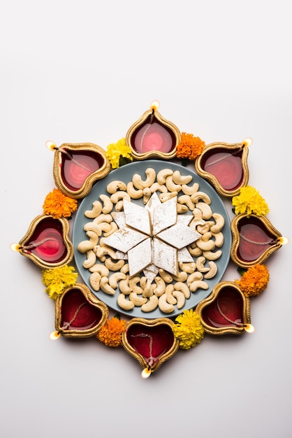 Cibo Diwali Rangoli usando Kaju Katli dolce insieme a Clay diya o lampada e fiori di calendula disposti in uno schema circolare, messa a fuoco selettiva