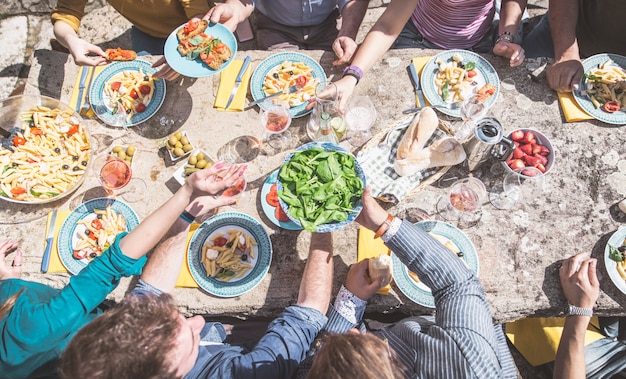 Cibo e amici. Gruppo di persone che mangiano varie cose all'aperto. Sopra la vista sul tavolo di pietra